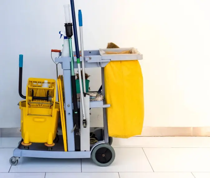 A yellow cart full of cleaning supplies from Atlas Janitorial Supplies in a room.