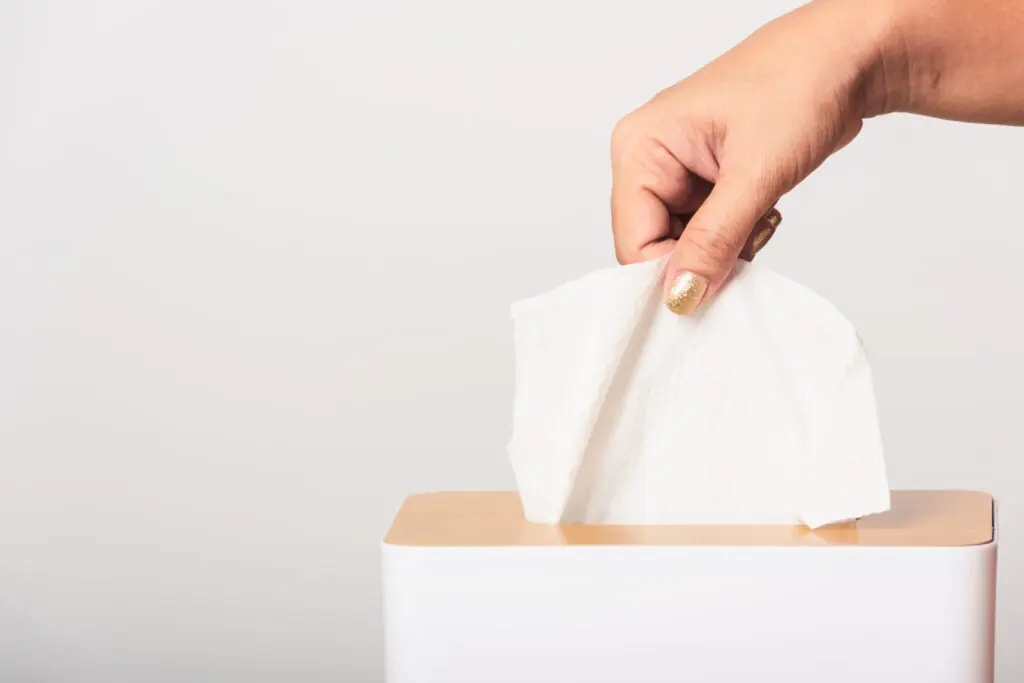 A hand putting a tissue into a box on a white background.